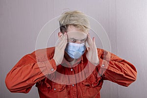 A teenager in a medical mask holds his head with his hands. Concept: headache, symptoms of coronavirus disease,