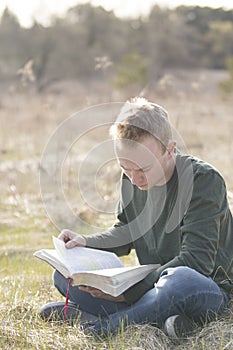 Teenager in open field reading Bible