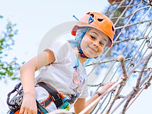 Teenager in orange helmet climbing in trees on forest adventure park