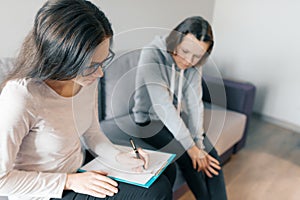 Teenager patient girl talking with professional psychotherapist in office.