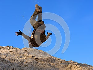 Teenager performs freerunning somersault on sand hill
