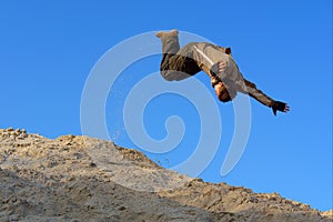 Teenager performs gliding jump on sand hill