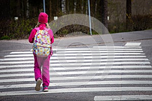 Teenager in a pink outfit with a cute backpack crossing the zebra on the street at daytime