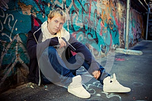 Teenager with a pistol sitting near graffiti wall