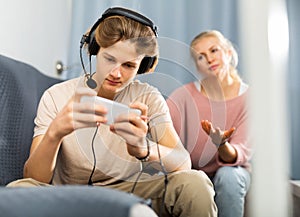 Teenager playing game on phone while upset mother talking to him