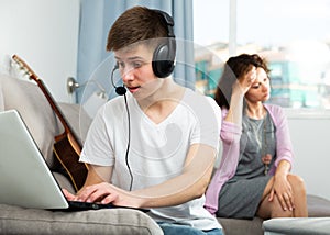 Teenager playing on laptop on background of worried mother