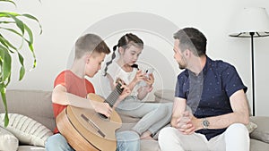 A teenager plays the guitar for his father and sister. A boy is learning to play the acoustic guitar