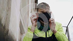 A teenager puts a black protective mask on his face while sitting on a metal ladder.