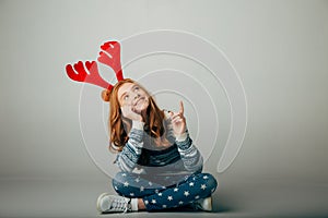 Teenager with red deer horns shows a good price for Christmas presents. Girl sitting smiling, as she sees discounts for