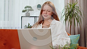 Teenager red hair girl sitting on home couch, making video conference call with friends or family