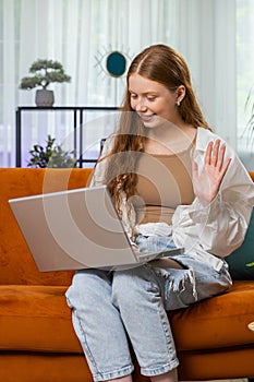 Teenager red hair girl sitting on home couch, making video conference call with friends or family