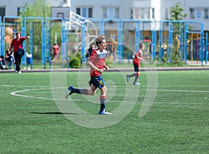 Teenager in red sportswear plays football on field, dribbles ball. Young soccer players with ball on green grass.