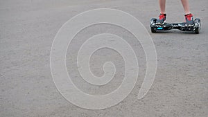 The teenager rides on a self-balancing two-wheeled hoverboard on the asphalt. The legs are close-up. Movement from the