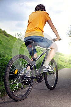 Teenager riding a bicycle on the road summer sunlit