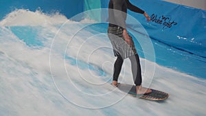 Teenager is riding surf board on wave simulator indoors. Young surfer during training on generated waves. Water sport