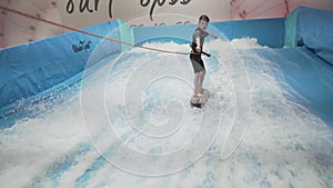 Teenager is riding surf board on wave simulator indoors. Young surfer during training on generated waves. Water sport