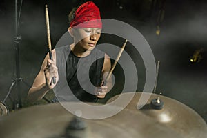 Teenager rock band drummer . cool and talented Asian American mixed ethnicity teenage boy playing drums in headband performing