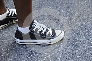 Teenager's feet in a pair of black canvas All-Stars casual shoes stands on urban asphalt road