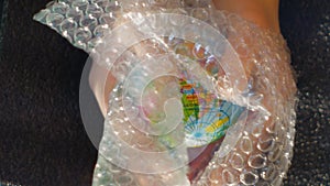 A teenager`s hand holds a small globe, above it appears a sheet of bubble wrap, ideal footage to represent ecology