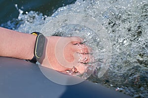 Teenager& x27;s hand with a waterproof fitness bracelet is lowered into the water