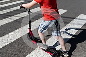 A teenager with a scooter crosses the road at a pedestrian crossing. Road safety