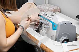 A teenager sews a brown dress on a sewing machine called an overlock.