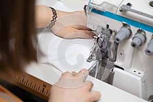 A teenager sews a brown dress on a sewing machine called an overlock.