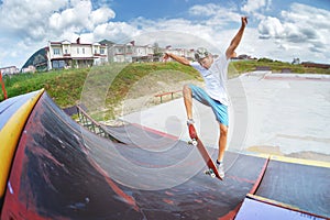 A teenager in shorts and a cap does an allie stunt on a ramp in a skate park in a residential area in summer. The