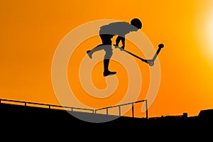 Teenager silhouette showing high jump tricks on scooter against orange sky