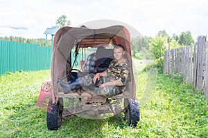 A teenager sits in the trailer of a makeshift all-terrain vehicle with a trailer.