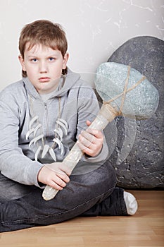 Teenager sits with unkind face with stone ax