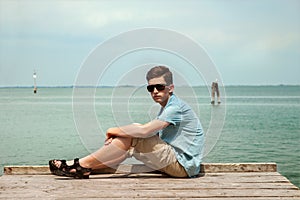 Teenager is sitting on the beach on a wooden pier
