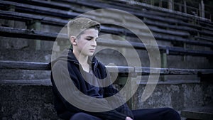 Teenager sitting on stadium tribune, devastation and poverty, city after war