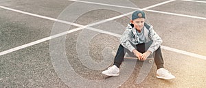 Teenager skateboarder boy with a skateboard sitting on asphalt playground and resting after he made tricks. Youth generation