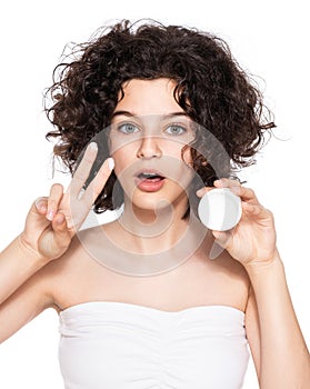 Teenager skincare. Beautiful teenage girl with gorgeous curly hair holding moisturiser face cream, looking at camera.