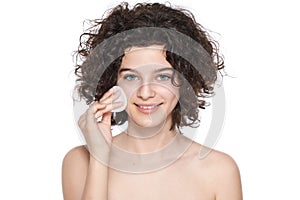 Teenager skincare. Beautiful teenage girl with gorgeous curly hair using cotton pad to remove make up, looking at camera smiling.