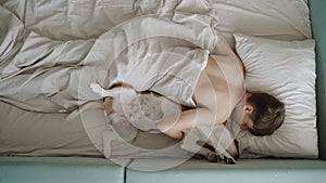 A teenager sleeps with his dog in bed. The dog is lying on its back, and it looks very funny.