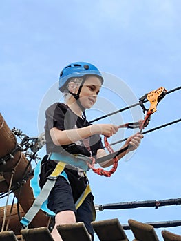 A teenager in sports equipment attaches a carabiner to a rope descent. View from below