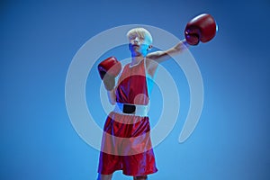 Teenager in sportswear boxing isolated on blue studio background in neon light