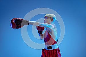 Teenager in sportswear boxing isolated on blue studio background in neon light
