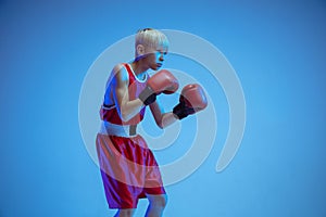 Teenager in sportswear boxing isolated on blue studio background in neon light