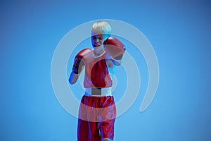 Teenager in sportswear boxing isolated on blue studio background in neon light