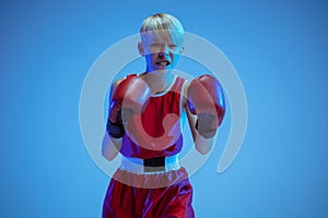 Teenager in sportswear boxing isolated on blue studio background in neon light