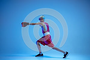 Teenager in sportswear boxing isolated on blue studio background in neon light