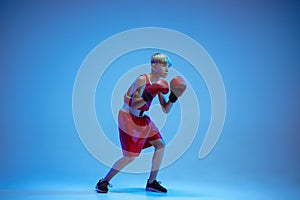 Teenager in sportswear boxing isolated on blue studio background in neon light