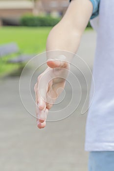 A teenager in sportswear extends his hand for a handshake and invites for a jog in the park