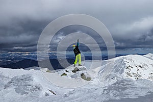 Teenager stands on the edge of mountain and celebrate hard climb of this mountain. Back view on man dressed in winter clothes.