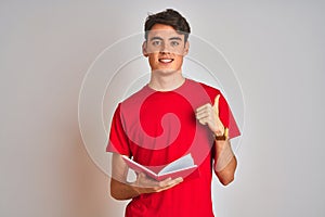 Teenager student boy reading a book over isolated background happy with big smile doing ok sign, thumb up with fingers, excellent