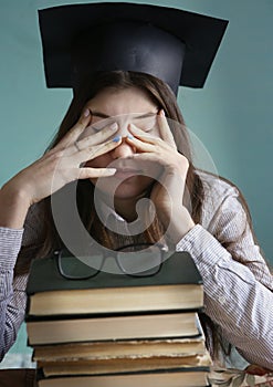 Teenager student girl in graduation cap with bood pile tired eyes