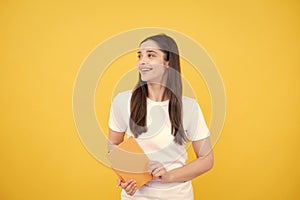 Teenager student girl isolated on yellow background. Cheerful young woman student in shirt hold notebooks showing. High